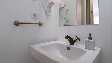 Un baño con un lavamanos blanco, un grifo de latón, un espejo y dos secadores de pelo montados en la pared.
