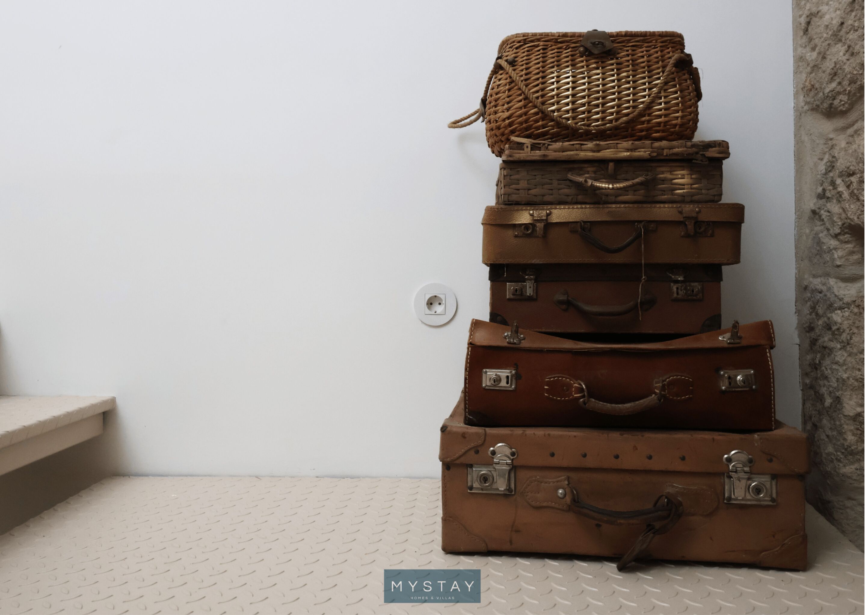A stack of vintage suitcases against a white wall with a textured floor.