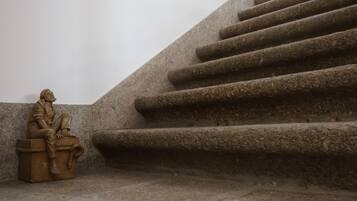 Una escultura de una figura sentada en un banco de piedra junto a una escalera.