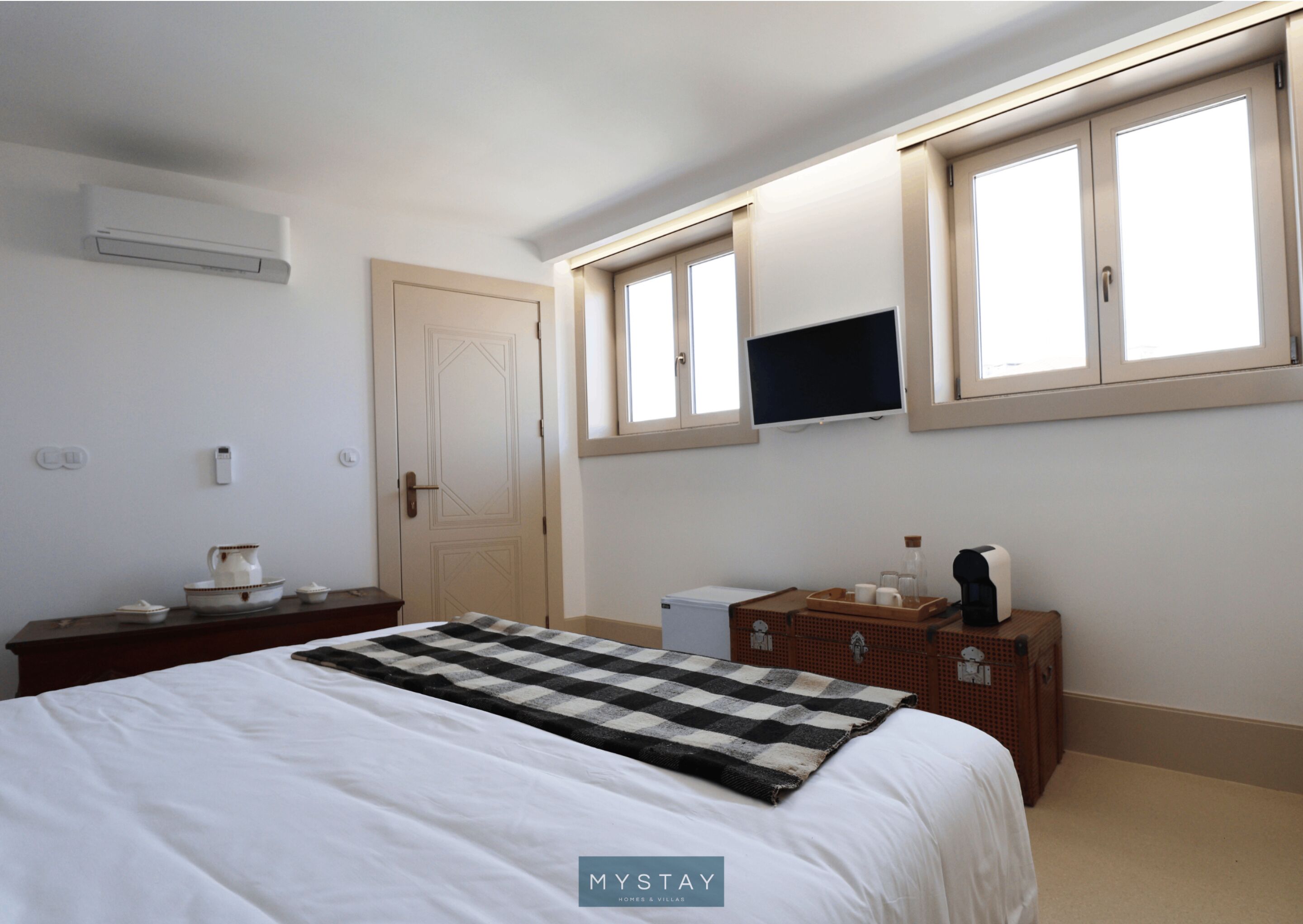 A bedroom with a bed, a TV mounted on the wall, a window, and a dresser.