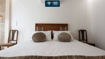 Un dormitorio con cama, dos almohadas, cabecera de madera, unidad de aire acondicionado montada en la pared y una pequeña mesa con silla.