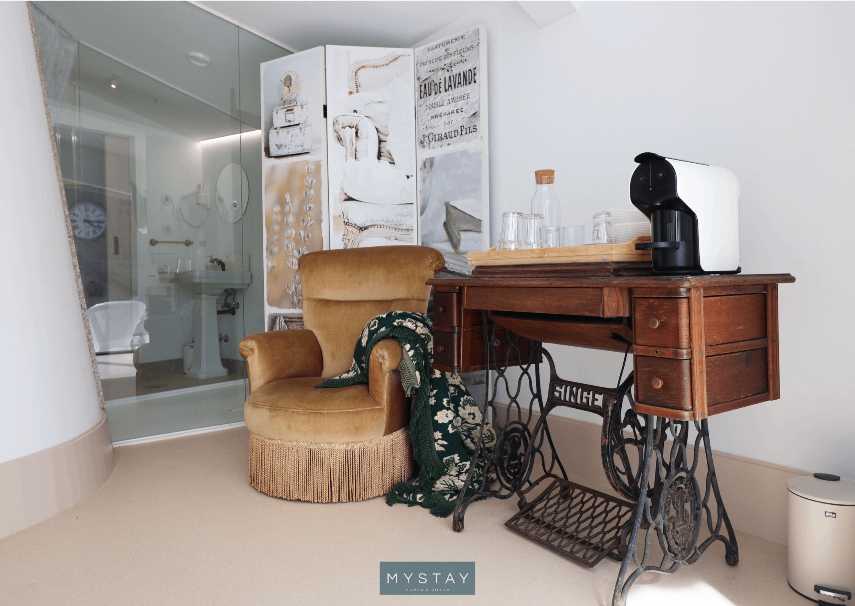 Una habitación con un escritorio tipo máquina de coser antigua, un sillón cómodo y un cartel decorativo.