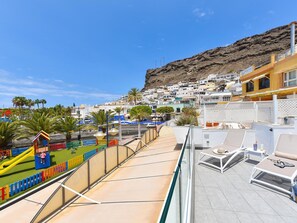A rooftop terrace with sun loungers and a view of a coastal town. - Apartment Mogan With Stunning Beach Views (Mogan)