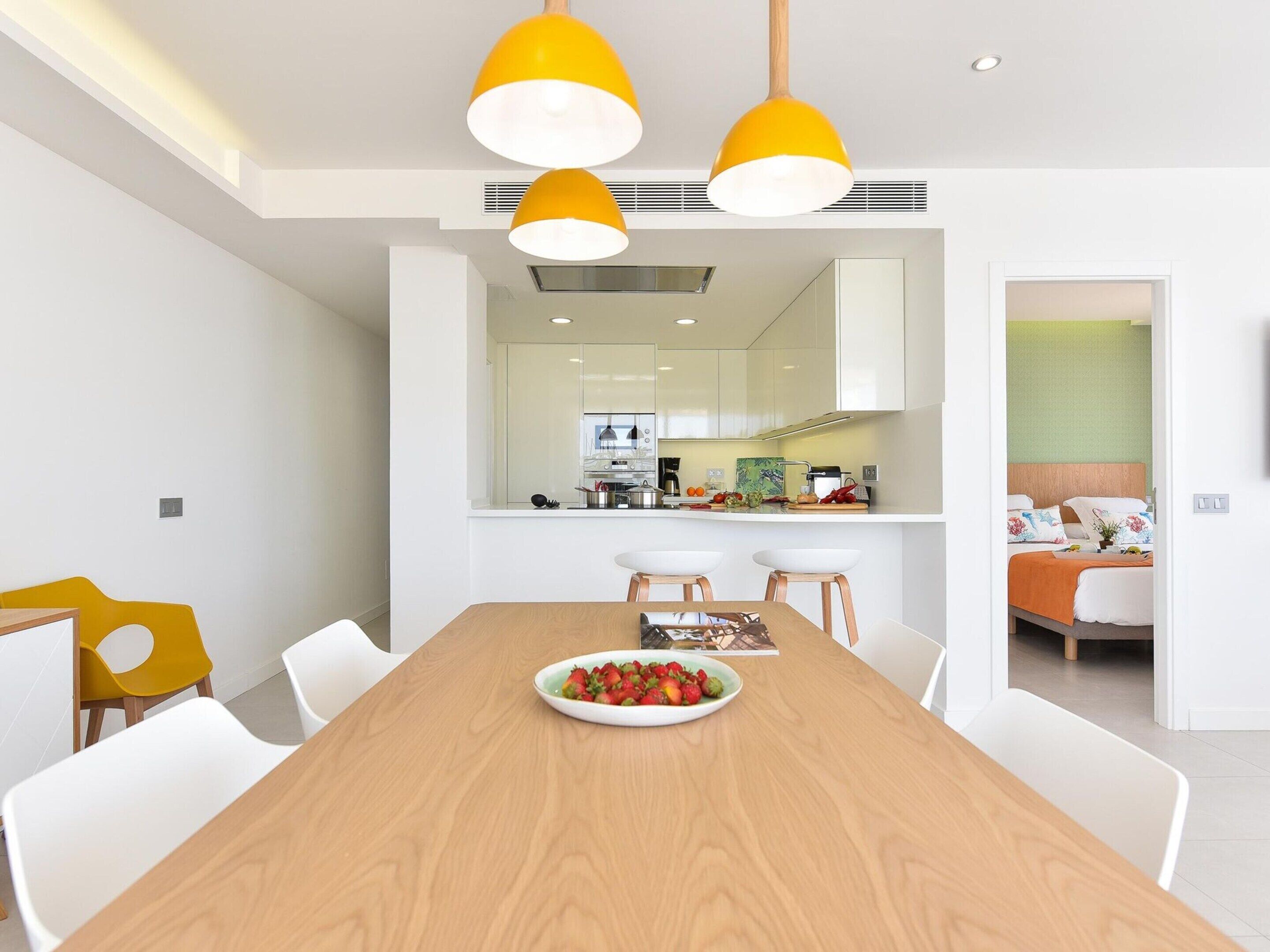 A modern kitchen with white cabinets, a central island, and a dining area with a wooden table and white chairs.