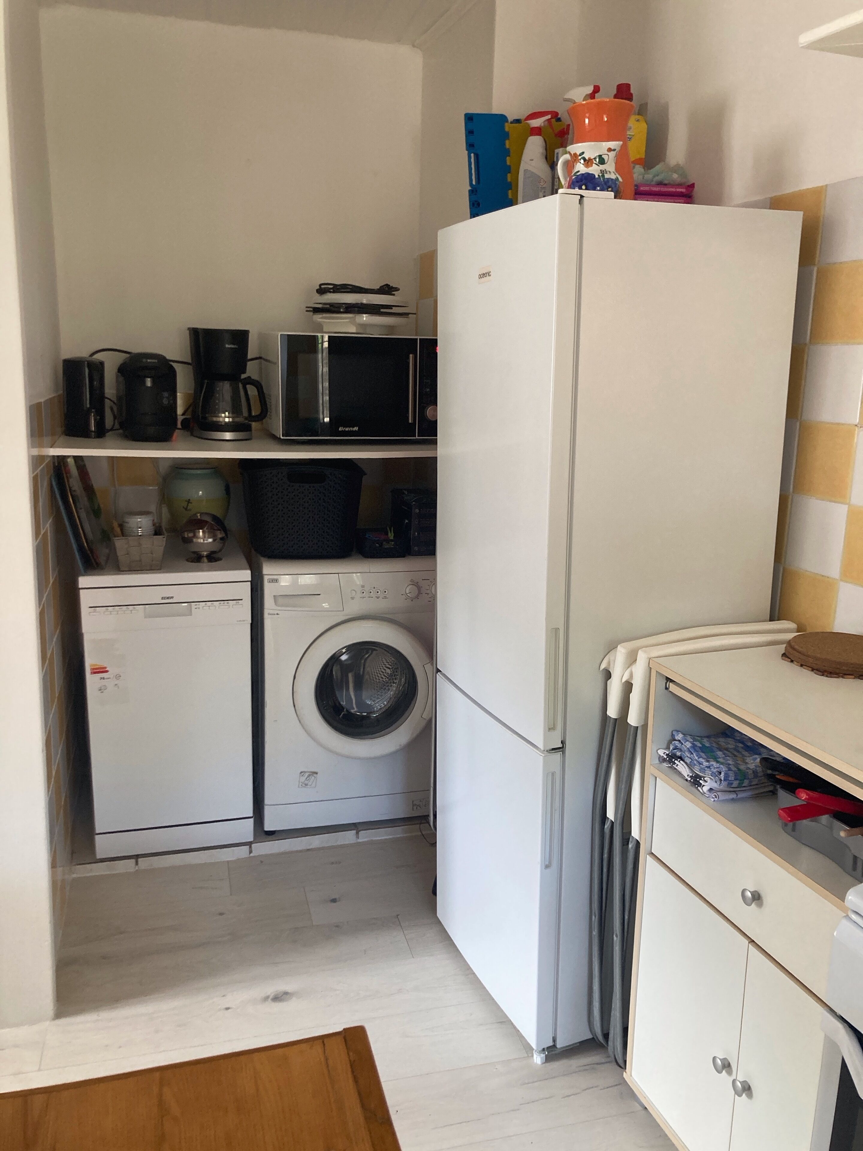 Een praktische keuken met een koelkast, magnetron, koffiezetapparaat en wasmachine.