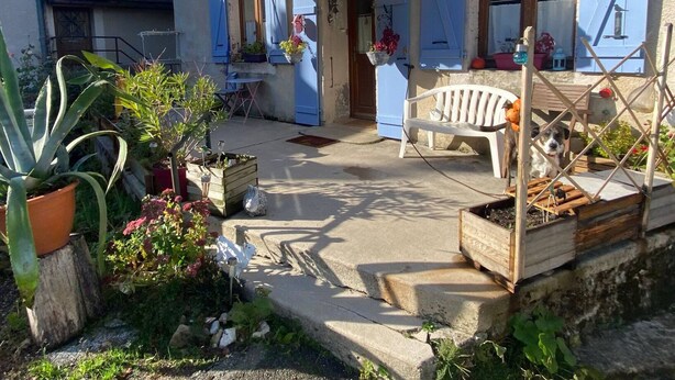 Ein rustikales Haus mit überdachter Veranda, einer hölzernen Bank und Kübelpflanzen.