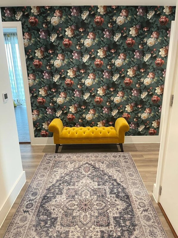 Ein Flur mit einem gelben, samtenen Sofa, einem gemusterten Teppich und blumigem Wandpapier.