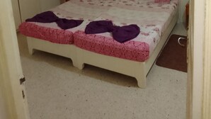 Ein kleines Zimmer mit einem Einzelbett, einem weißen Bett und einer rosa-weißen Bettdecke sowie einer violetten Decke.