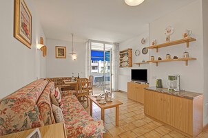 A living room with a sofa, a dining table, and a kitchen area with a TV and coffee maker.