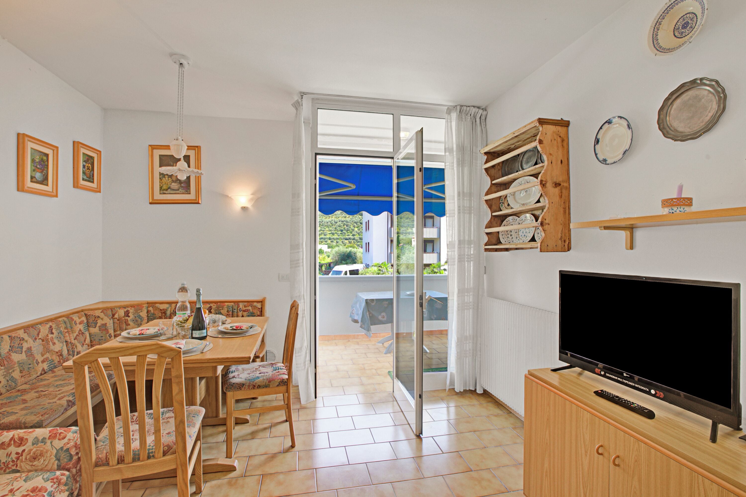 Comedor con una mesa y sillas, un televisor sobre un mueble de madera, y vista al exterior a través de un ventanal.