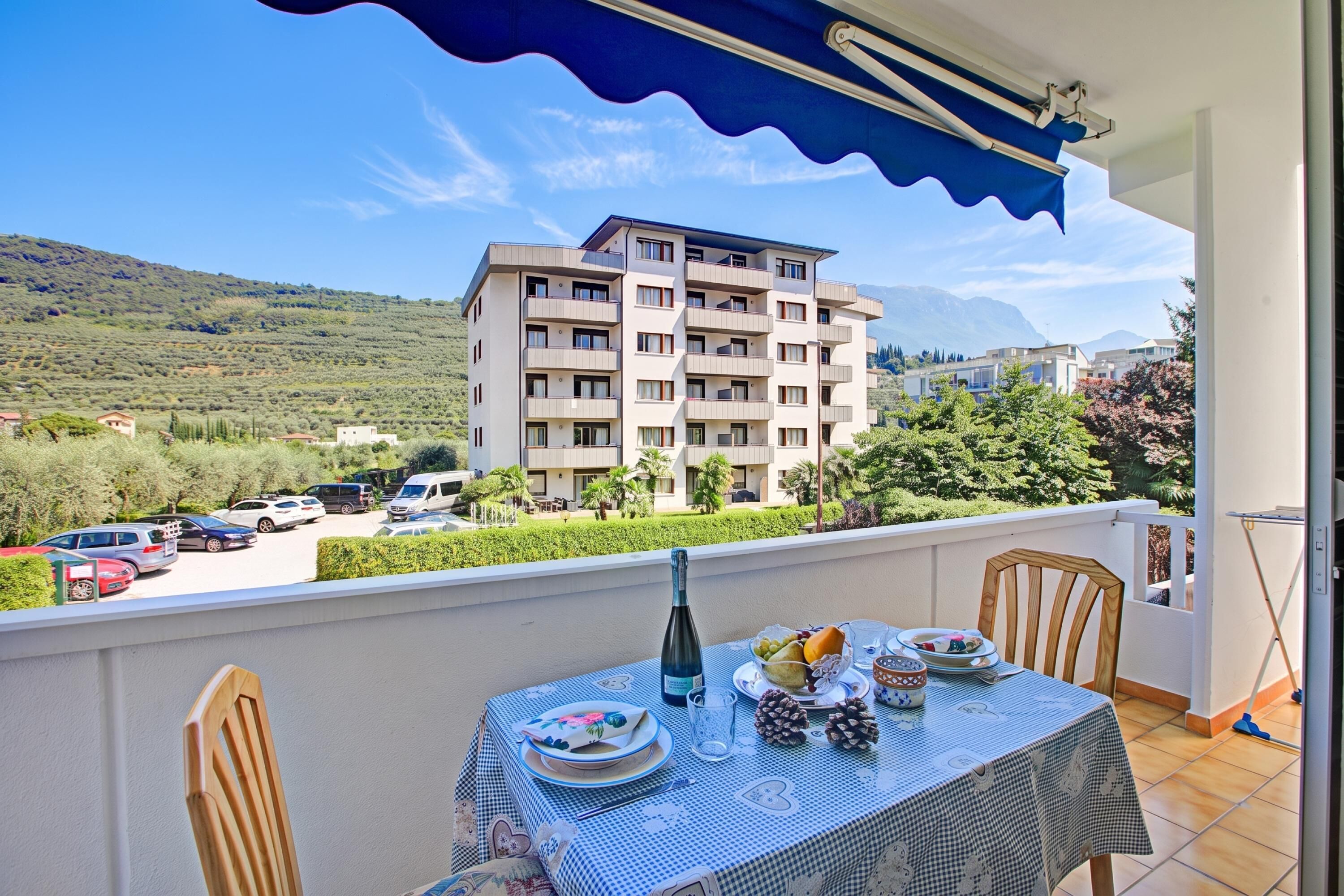A balcony with a table set for dining, overlooking a parking area and a multi-story building with balconies.