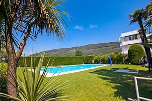 A swimming pool surrounded by well-maintained grass, a clear blue sky, and a hilly landscape in the background.