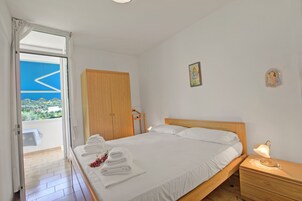 A bedroom with a bed, a nightstand, a wooden wardrobe, and a balcony with a view.