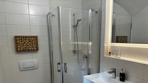 A modern bathroom with a glass-enclosed shower, a white sink with a wooden countertop, and a large mirror above the sink. - Bauer Wirt`s Zwei-zimmer-wohnung (Kirchham)
