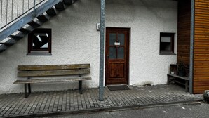 A building with a wooden bench, a door, and a small window. - Bauer Wirt`s Zwei-zimmer-wohnung (Kirchham)