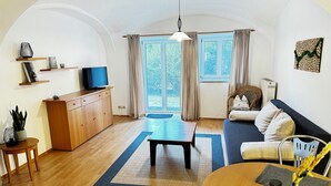 A spacious living room with a wooden floor, a sofa, a coffee table, and a TV on a wooden cabinet. - Bauer Wirt`s Zwei-zimmer-wohnung (Kirchham)