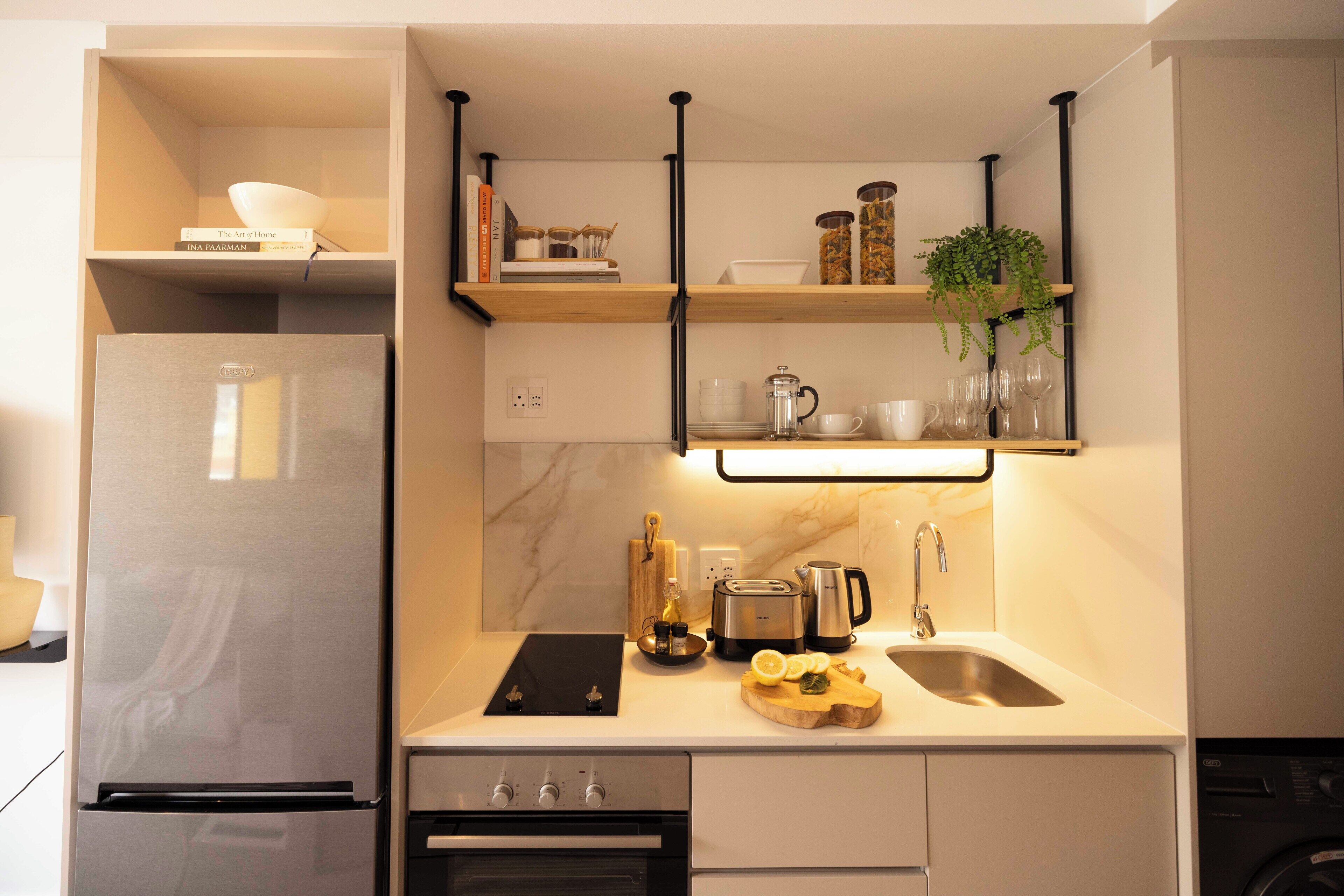 Eine moderne Küche mit Edelstahlkühlschrank, einem Backofen, einer Spüle und einer Arbeitsplatte mit Kaffeemaschine, Toaster und Schneidebrett mit Zitronenscheiben.