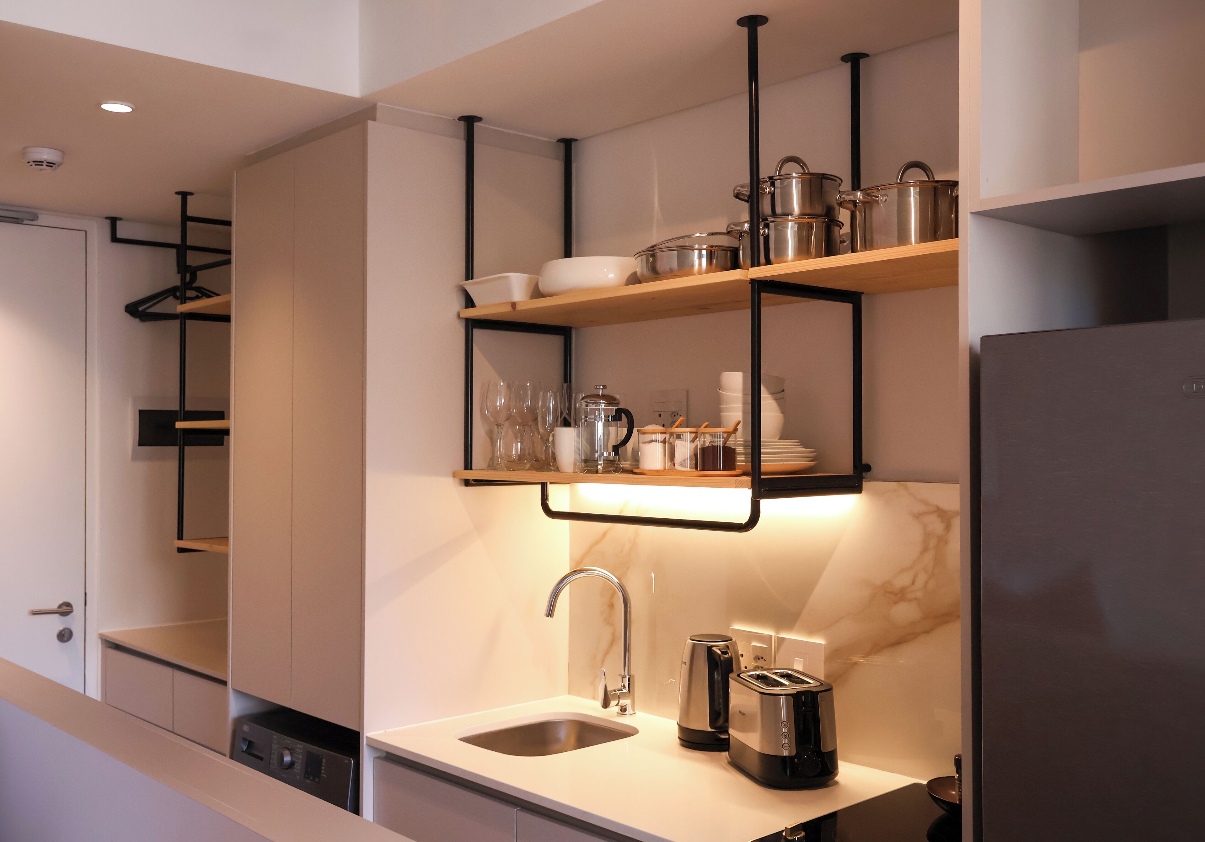 Una cocina moderna con lavavajillas incorporado, un fregadero y una cafetera. Hay estantes sobre el fregadero con vajilla y vasos.