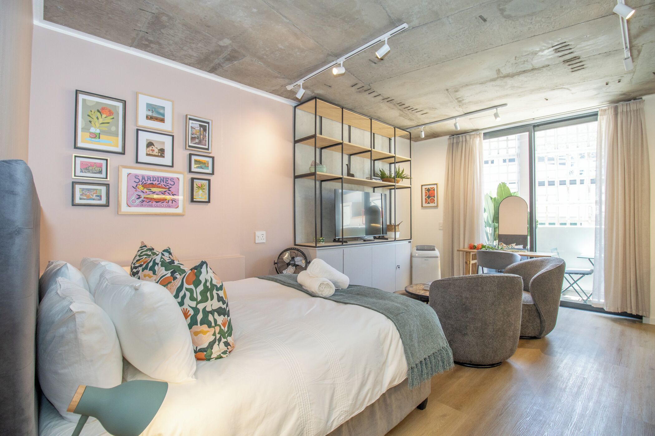 A modern bedroom with a bed, a desk, and a chair. There are framed pictures on the wall and a window with curtains.