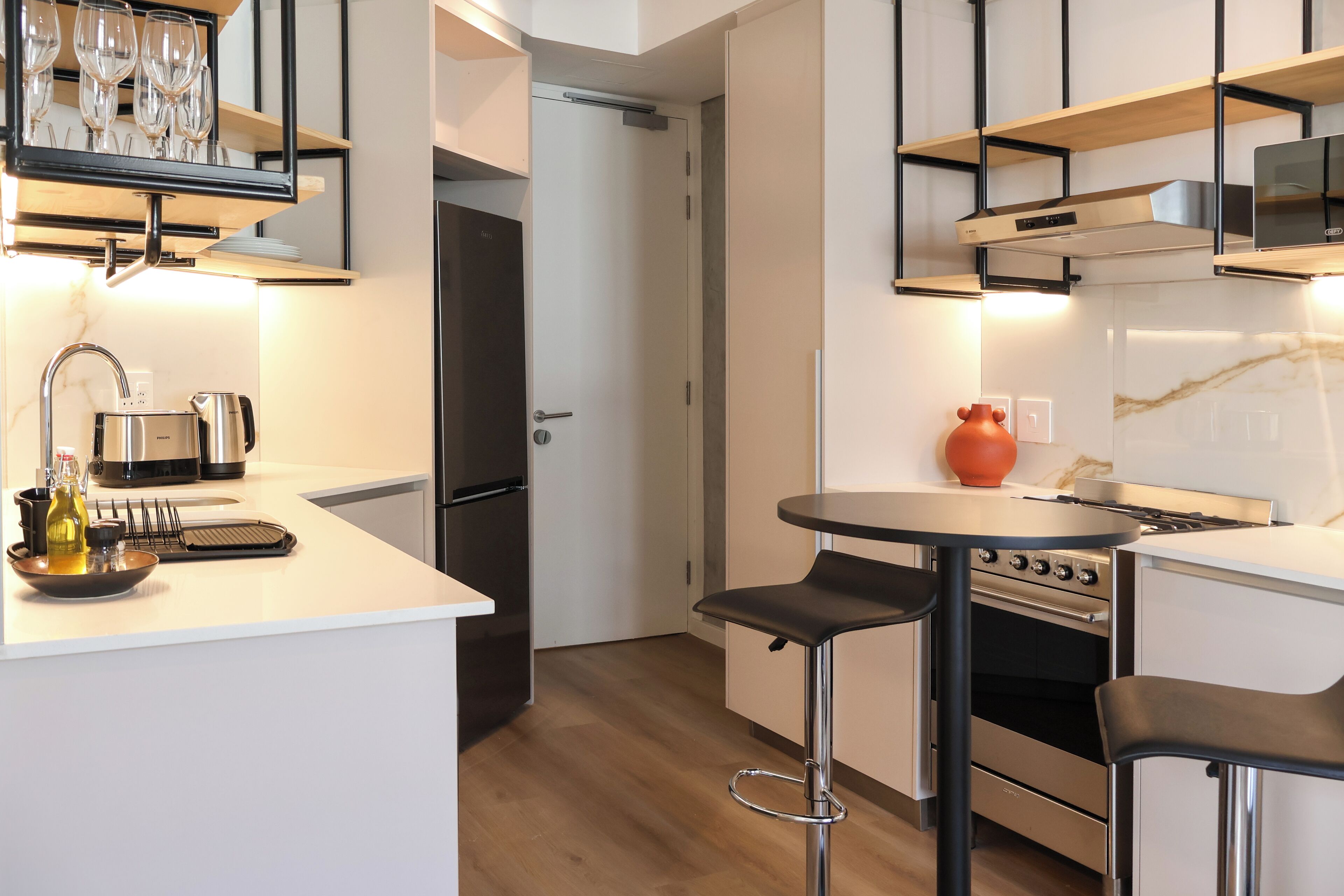 A modern kitchen with white cabinetry, a stainless steel stove, and a small dining area with a round table and two bar stools.