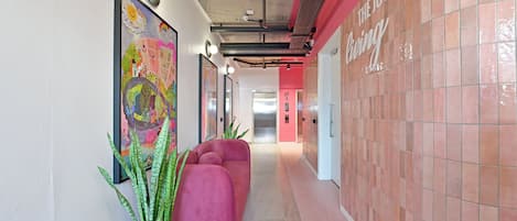A hallway with a pink sofa, a green plant, and a colorful mural on the wall.