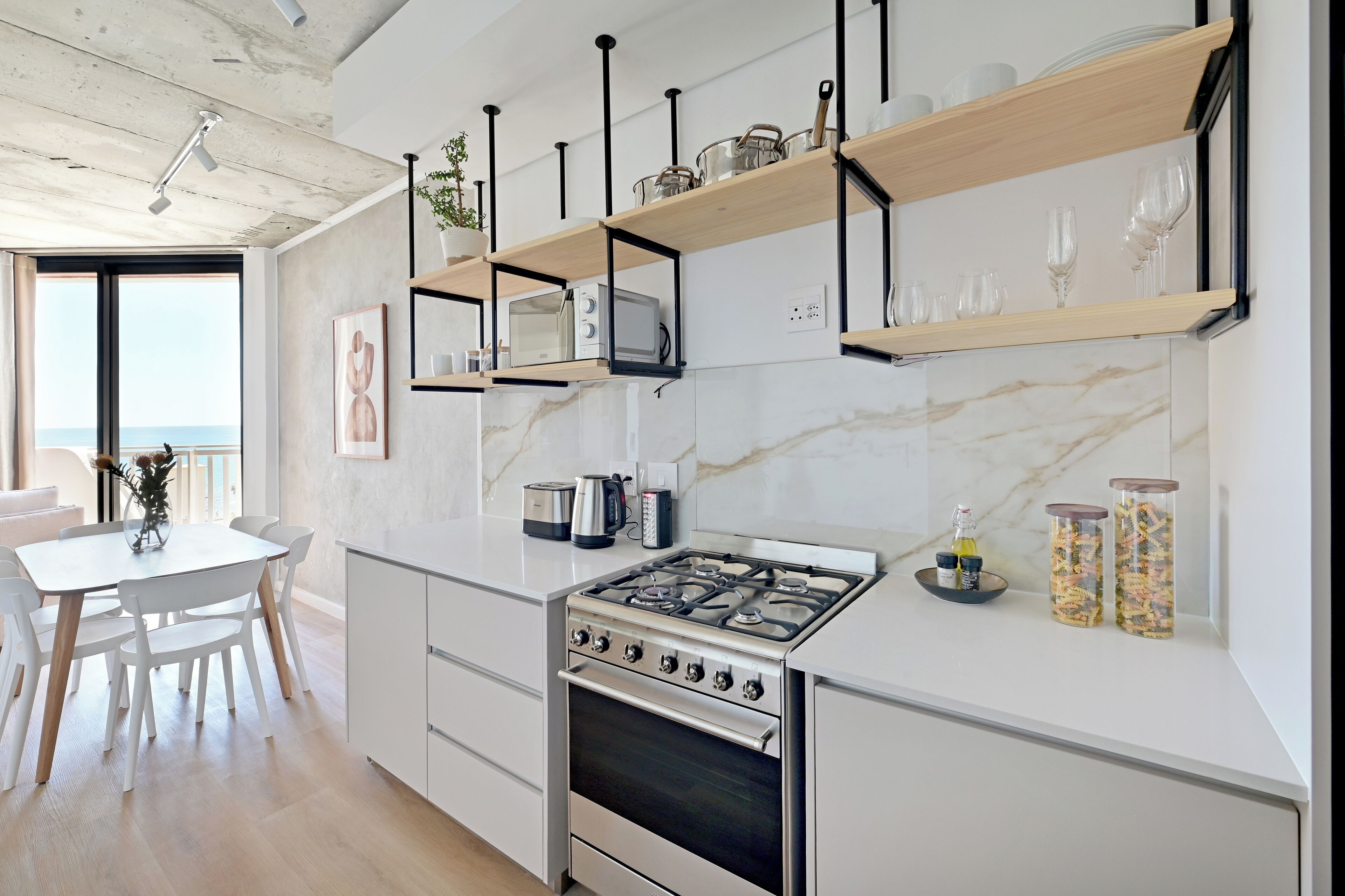 A modern kitchen with a gas stove, white cabinets, and wooden shelves.