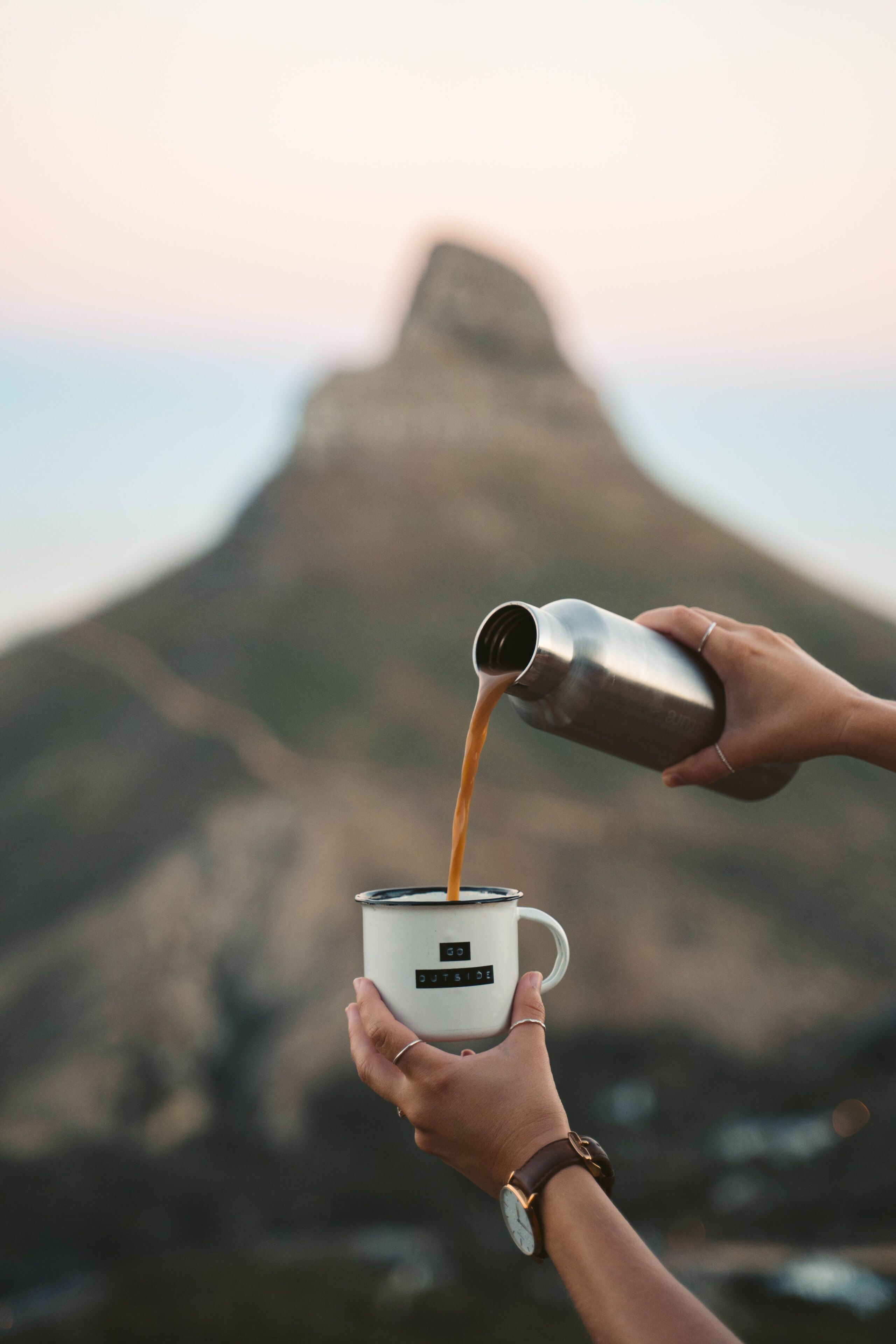 A person pouring a beverage into a mug with a label that reads 'OUTSIDE.'