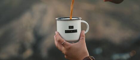 A person pouring a beverage into a mug with a label that reads 'OUTSIDE.'