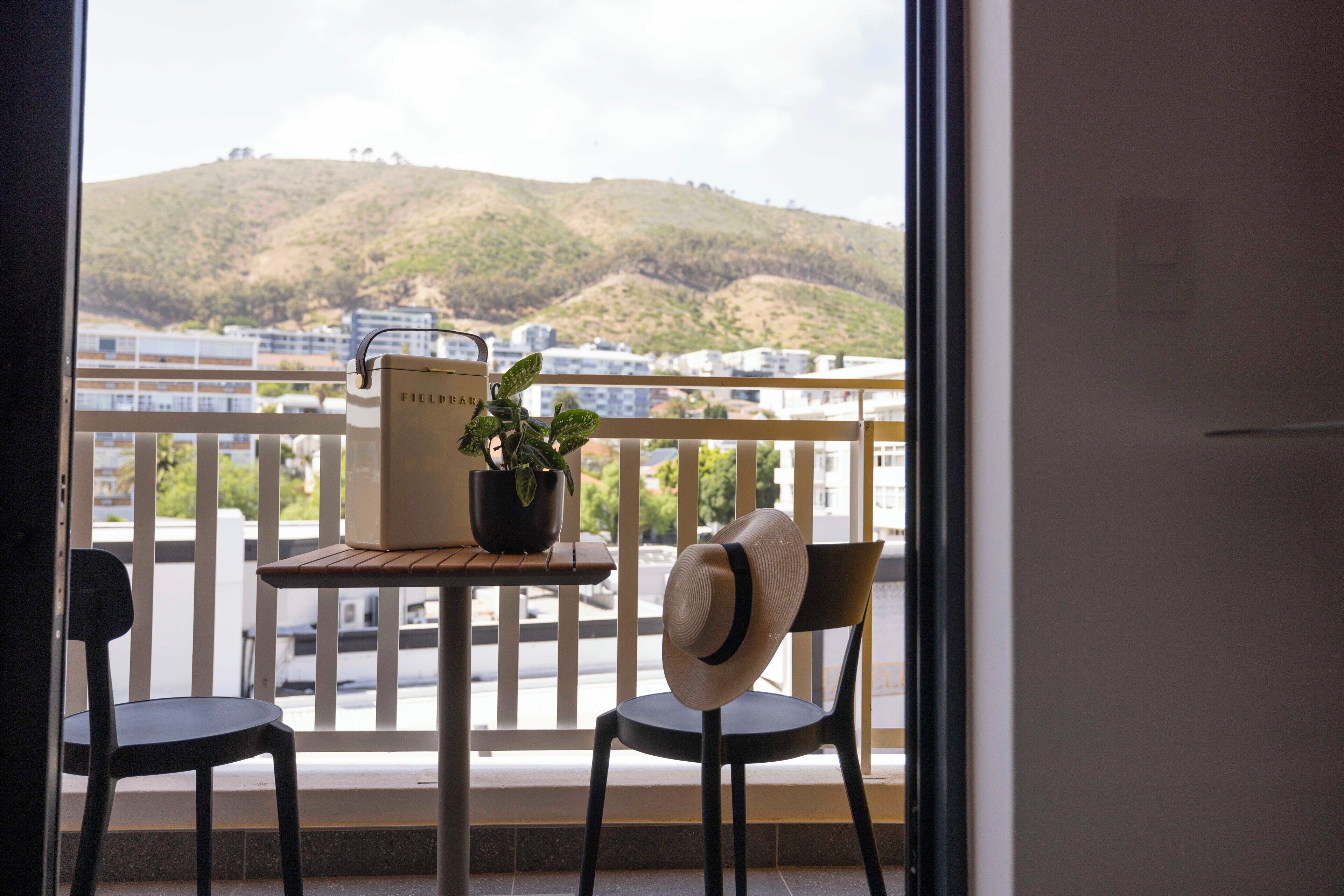 Een balkon met een tafel, twee stoelen, een bloempot en een koffer.