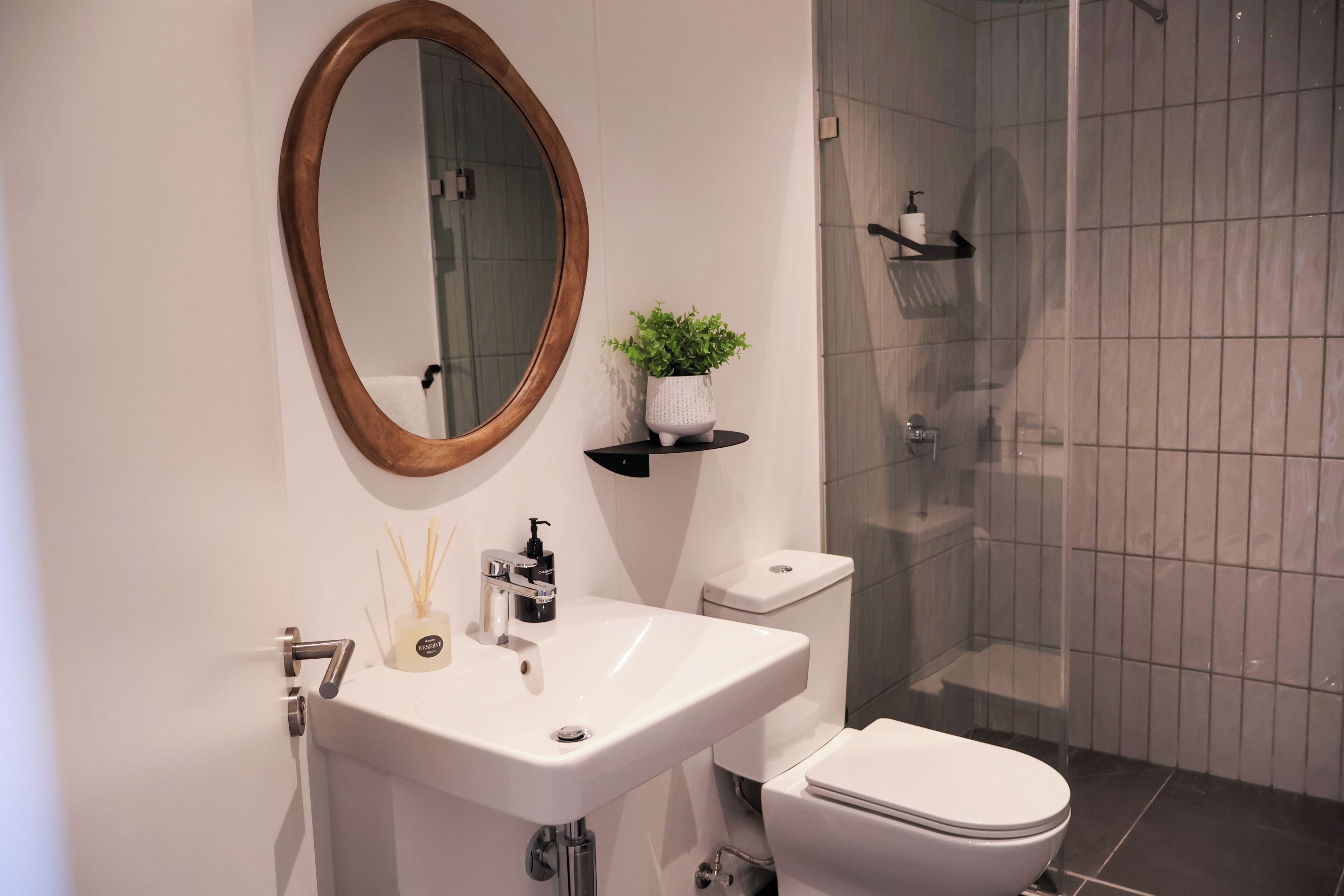 Un bagno moderno con un lavandino bianco, un water, cabina doccia in vetro e uno specchio con cornice in legno.
