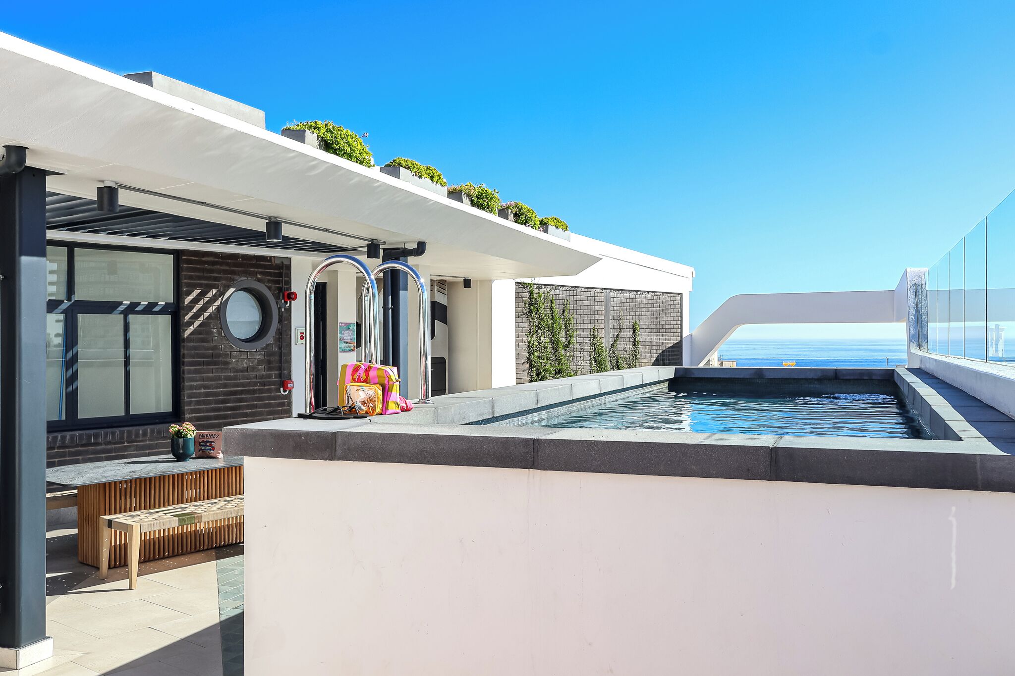 Una terraza moderna en la azotea con piscina, zona de estar y vistas al mar.
