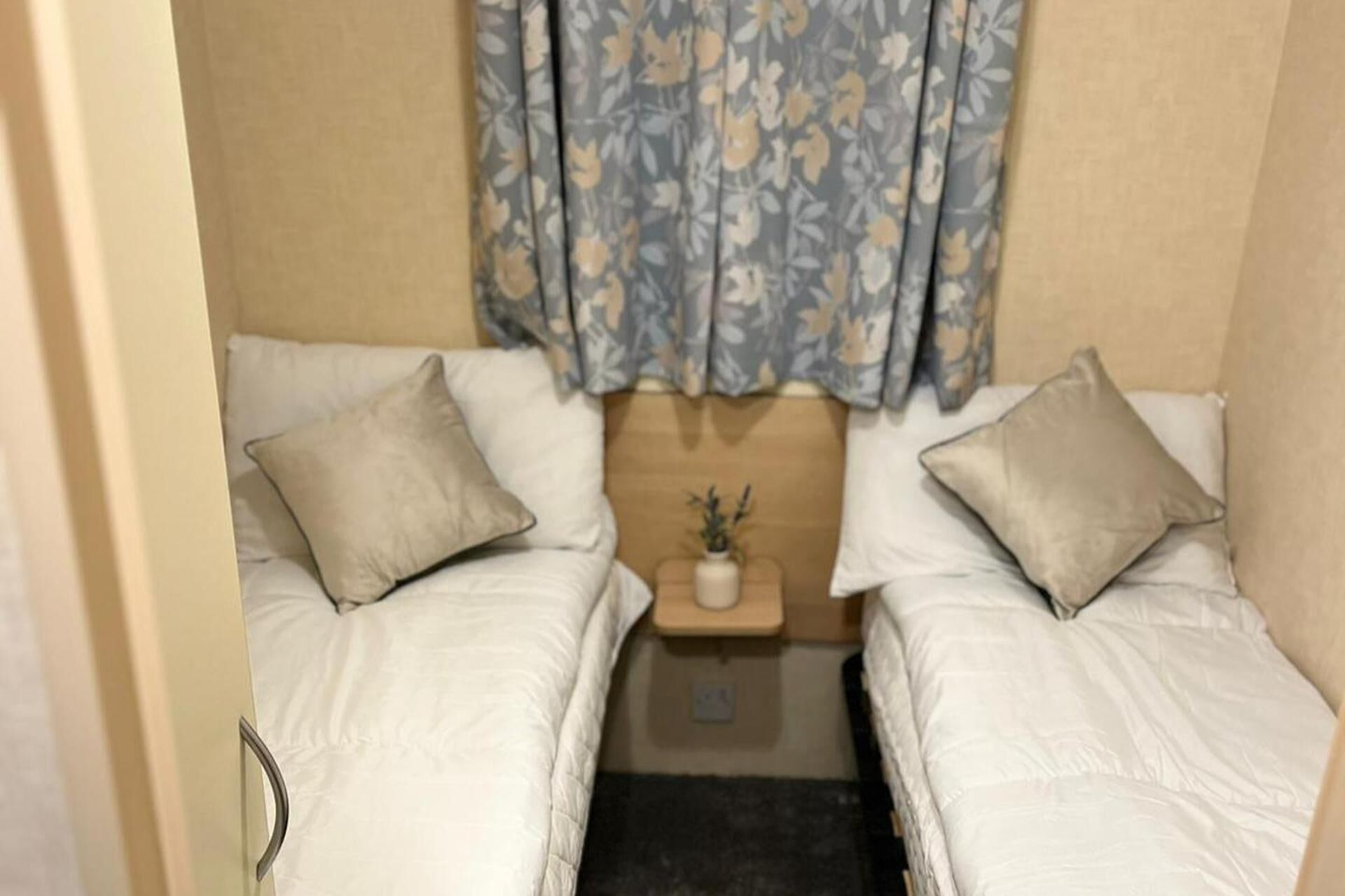 Una habitación pequeña y funcional con dos camas individuales, cada una con una almohada y una mesita de noche.