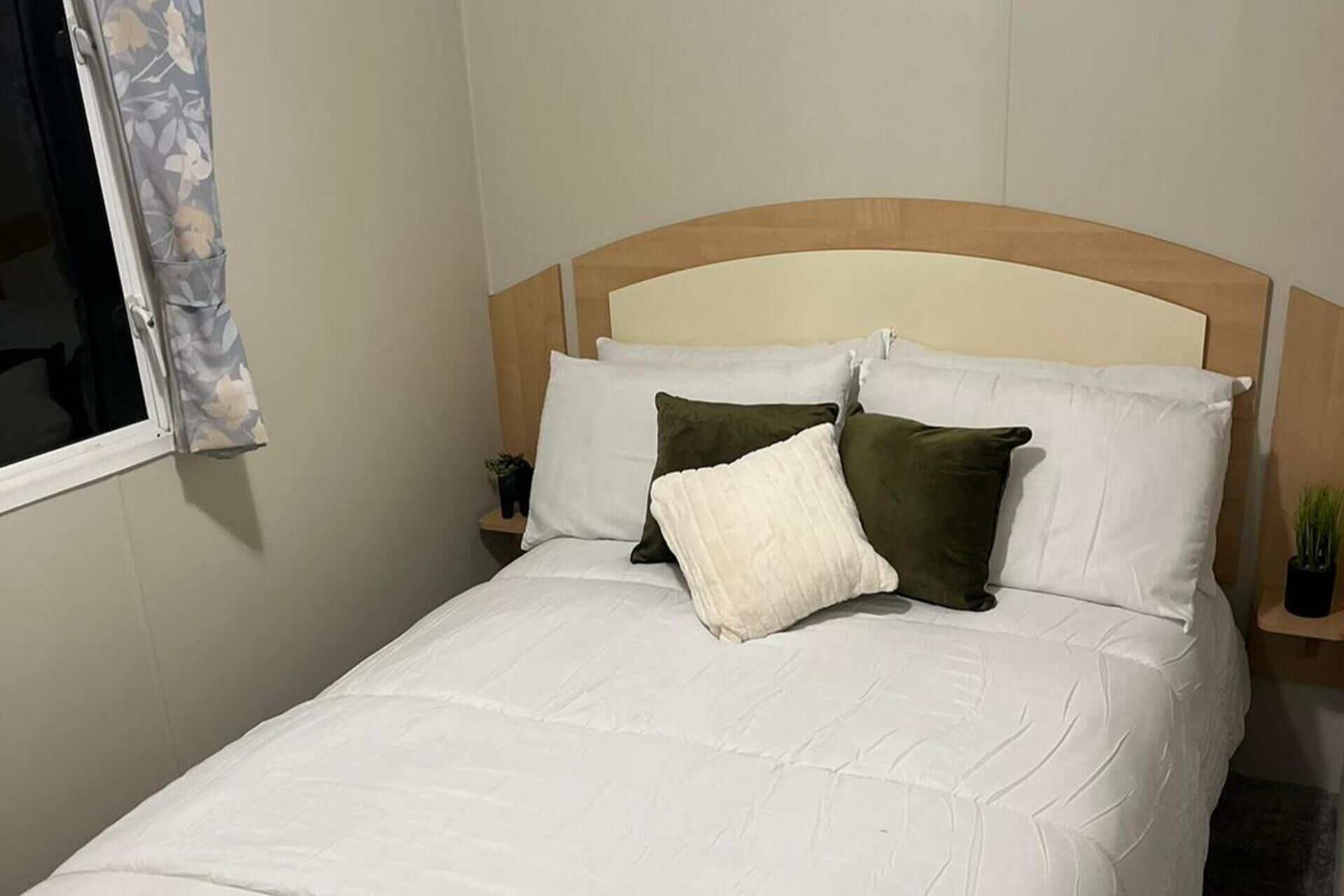 Ein Bett mit weißer Bettwäsche, zwei Kissen und einem hölzernen Kopfteil.