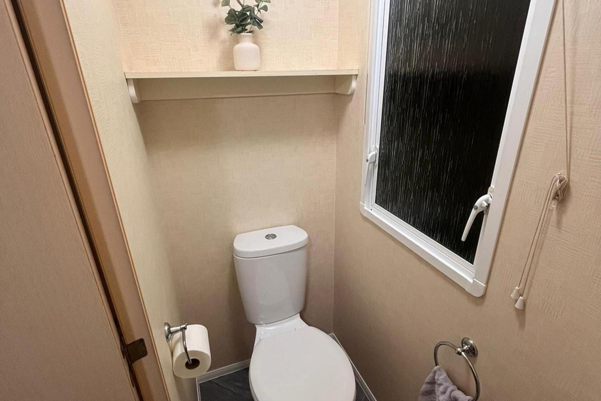 A small bathroom with a toilet, a towel rack, and a window.