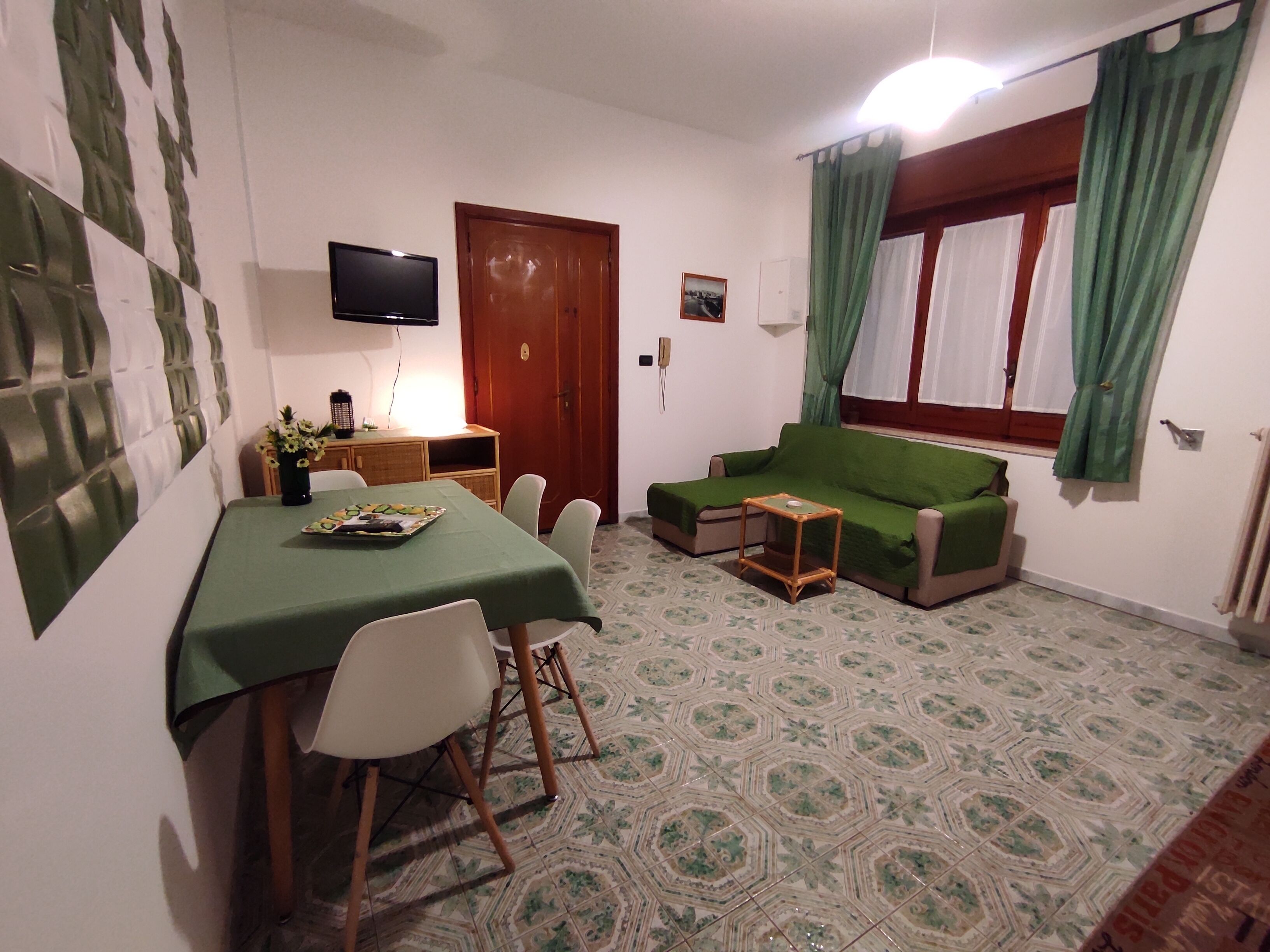 En kompakt opholdsstue med spisebord, stole, sofa, fjernsyn og et mønstret gulv.