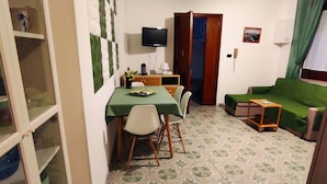 A compact living space with a dining area, a green sofa, and a television. - A few steps from beaches and center! (Otranto)