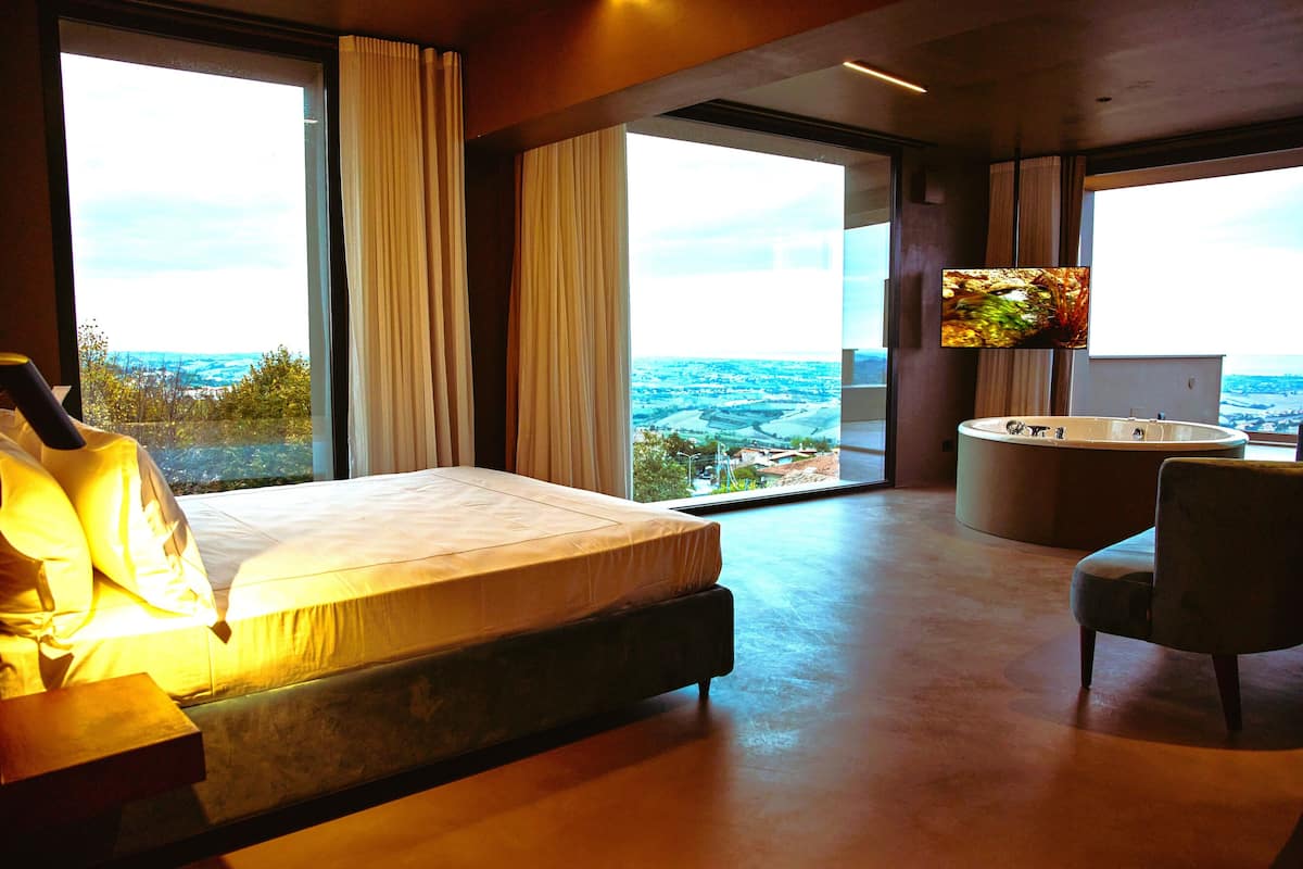 A modern hotel room with a large bed, a sitting area, a bathtub, and a TV.