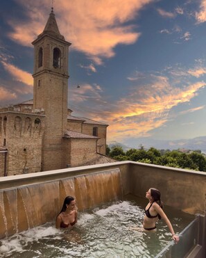 A historic building with a bell tower, a rooftop pool with water features, and a scenic view of the surrounding landscape. - LE AGAVI LUXURY RESORT&SPA (Saludecio)