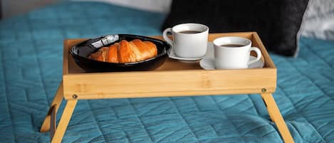 Una bandeja con croissants, dos tazas de café y un bol negro sobre una cama con colcha azul.