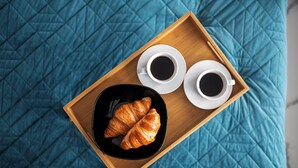 Una bandeja de madera con dos tazas de café y un croissant sobre un edredón acolchado azul.