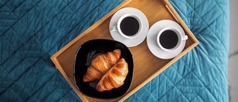 Una bandeja de madera con dos tazas de café y un croissant sobre un edredón acolchado azul.