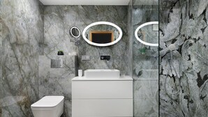 Un baño moderno con pared de mármol, un lavamanos blanco, un inodoro y una cabina de ducha con paredes de vidrio.