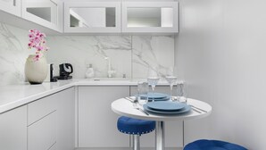 Una cocina moderna con armarios blancos, salpicadero de mármol y un comedor con una mesa redonda para dos.