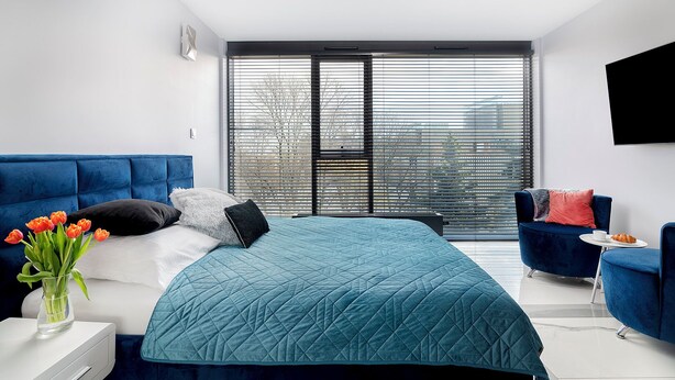 Un dormitorio moderno con una cama grande, un sofá azul y vistas de la ciudad a través de amplias ventanas.