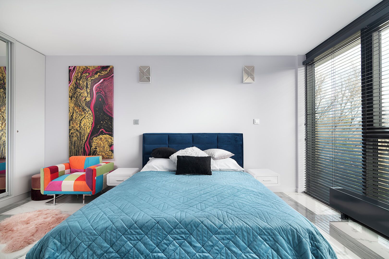 A modern bedroom with a large bed, a colorful chair, and a large abstract painting on the wall.