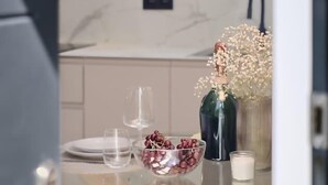A modern kitchen with a glass dining table, a bowl of grapes, a vase with flowers, and a hanging pendant light. - Romantic Apartment N2 Oceanografico Virkin Suites (València)