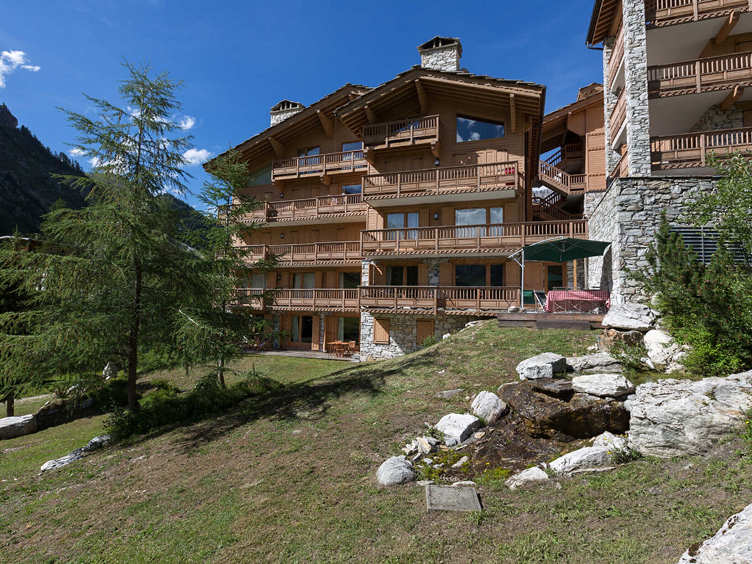 A multi-story lodge with balconies, stone walls, and a mountainous backdrop.