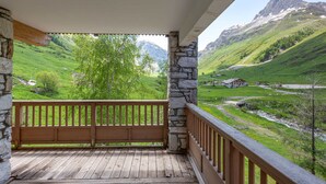 A wooden balcony with stone pillars, overlooking a green valley and mountains. - Luxurious Chalet-Style Apartment, South-Facing Terrace, Ski-In/Ski-Out, Val-d'Isère (Val-d'Isère)