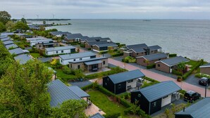 Zona residencial con casas modernas, un puerto deportivo y aerogeneradores al fondo.