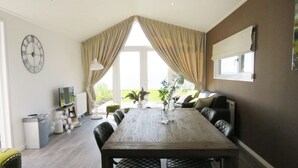 Un comedor moderno con una mesa de madera, sillas negras con cojines y un amplio ventanal con cortinas.